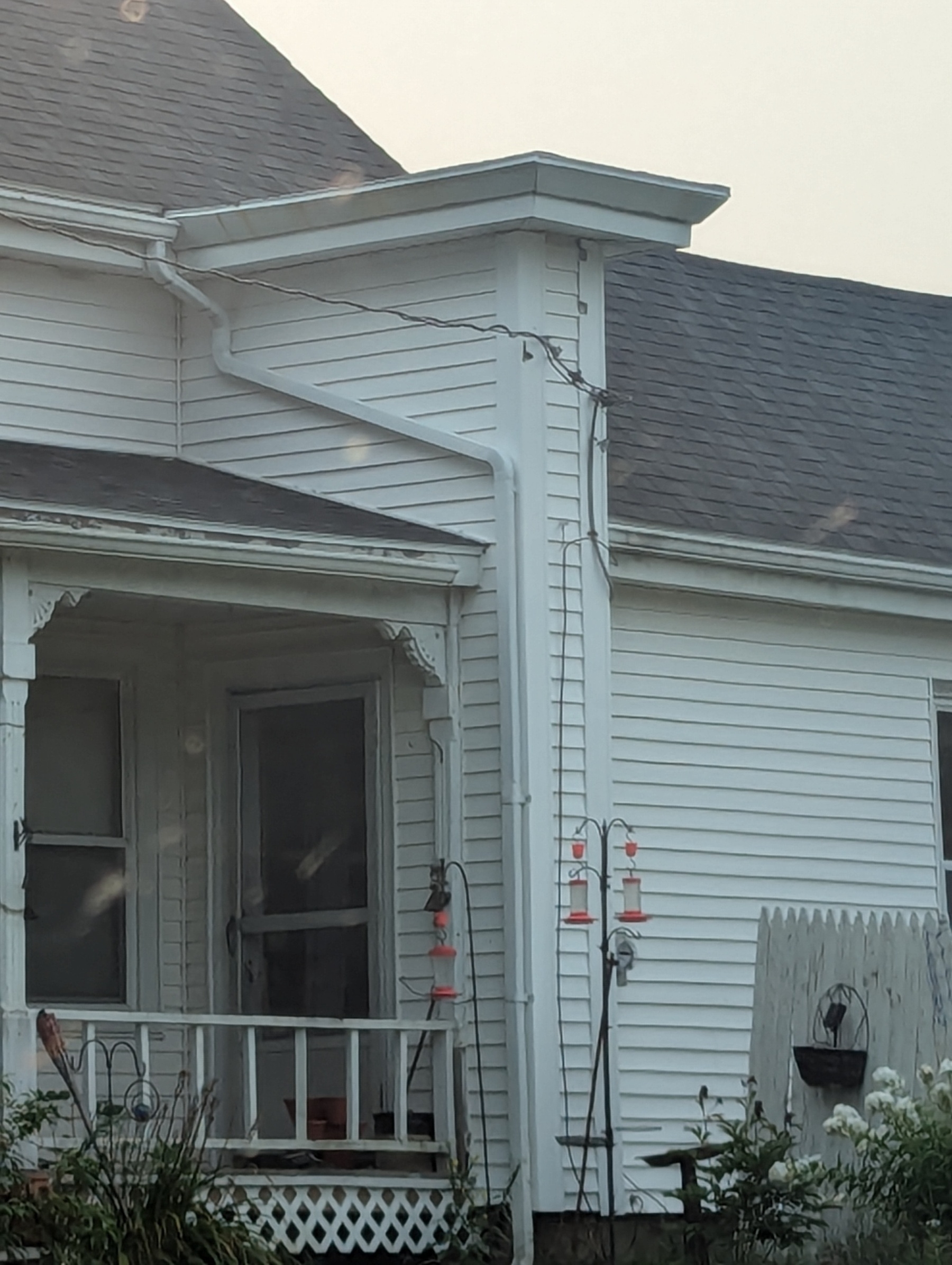 A white house with a small porch, featuring hummingbird feeders hanging near the entrance.